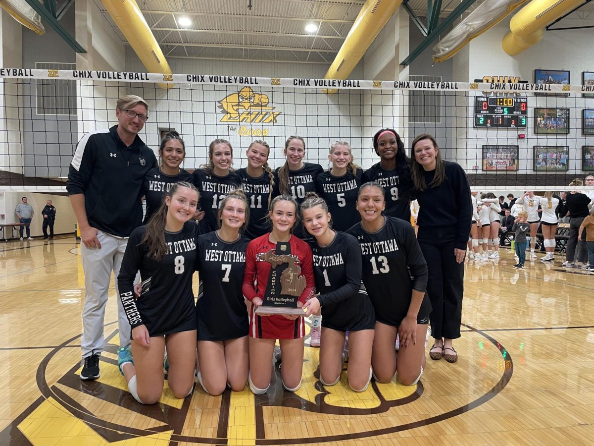 The West Ottawa Girls' Varsity volleyball team poses with the District Championship trophy as Chris Scholten snaps a picture.